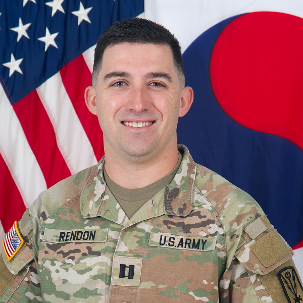 Captain Phillip Rendon smiles at the camera with two flags behind him.